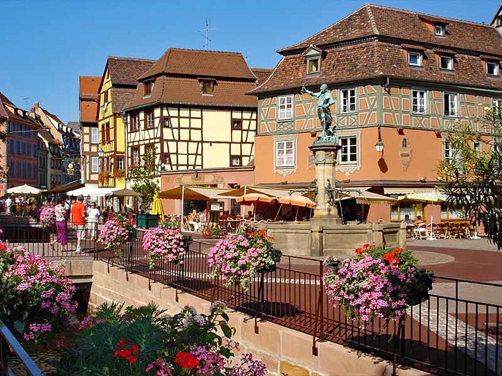 Schwendi Platz mit Brunnen, mit Blumen geschmückte Geländer, Gastgärten mit Sonnenschirmen