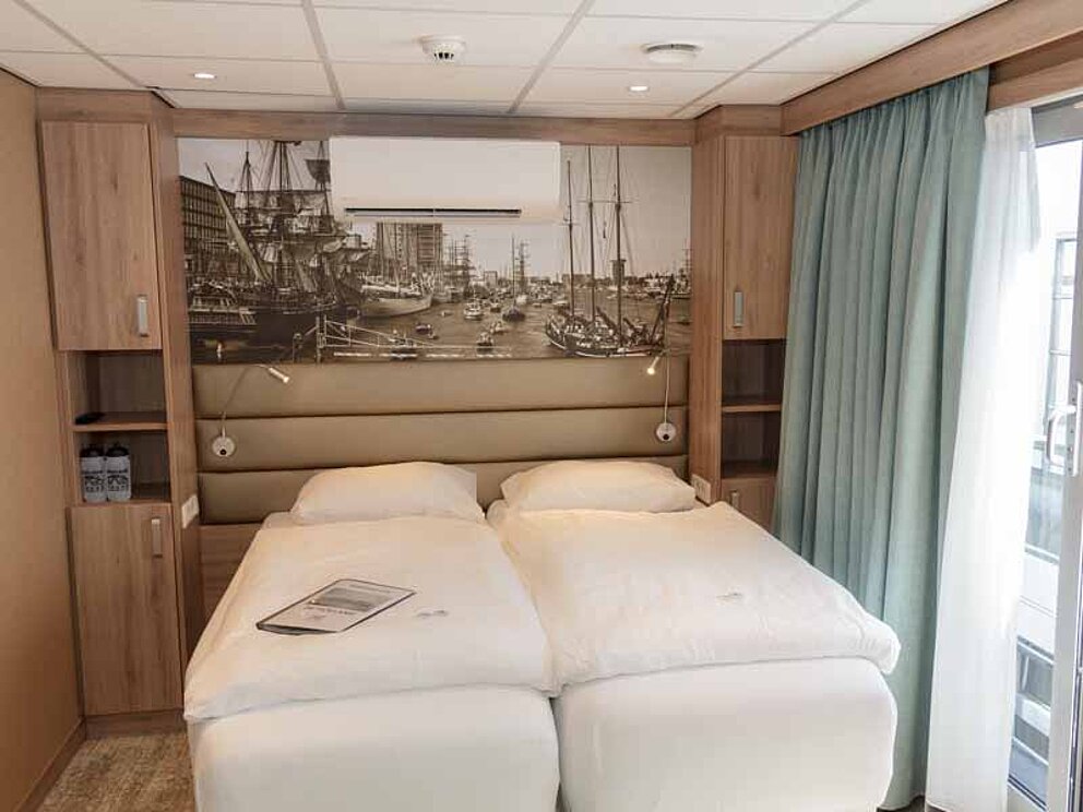 Kabine mit Twin-Betten. Dahinter ein Wandbild mit Hafen