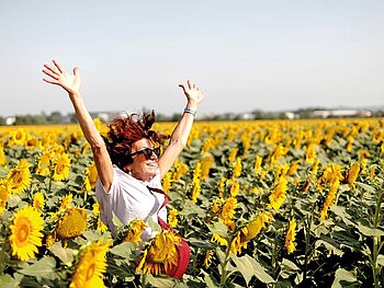 eine Dame steht inmitten eines Sonnenblumenfeldes. Alle Blüten sind aufgeblüht.