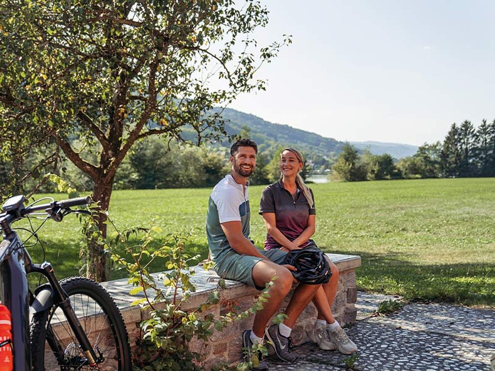 ein Paar sitzt auf einer Mauer im Schatten eines Obstbaumes.
