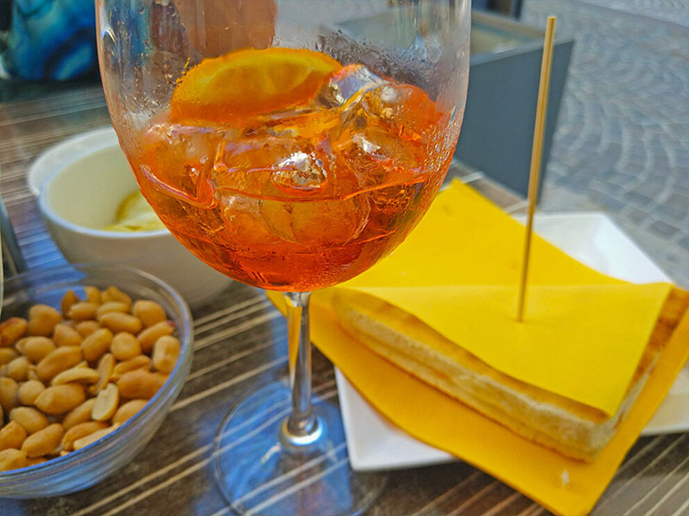 ein Glas Aperol Sprizz, eine kleine Schüssel mit Nüssen und ein Toast