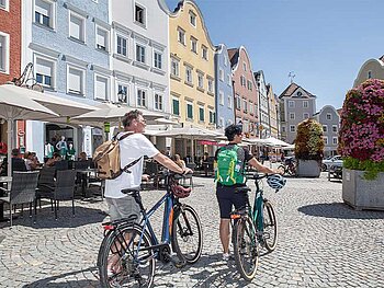 2 Radfahrer von hinten, im Hintergrund die bunte Silberzeile am Schärdinger STadtplatz