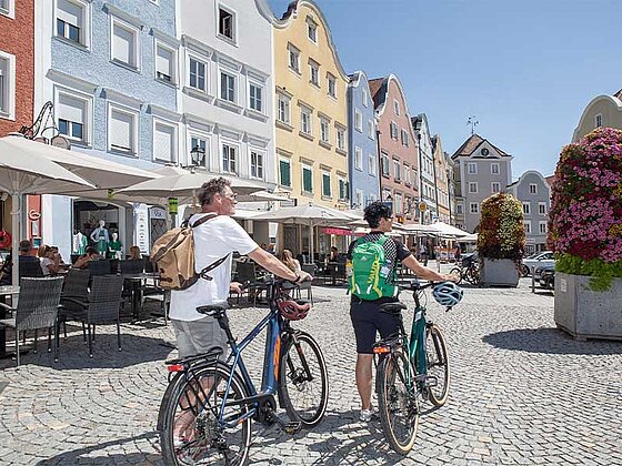 2 Radfahrer von hinten, im Hintergrund die bunte Silberzeile am Schärdinger STadtplatz