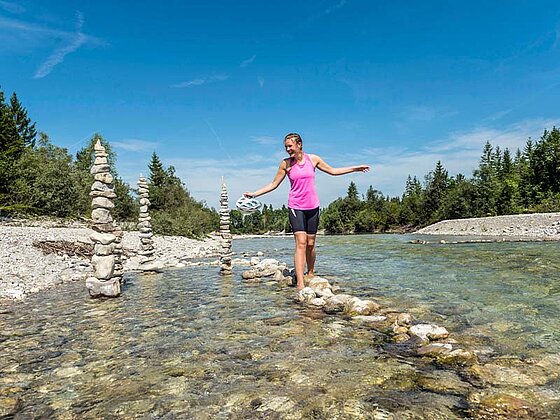Dame balanciert auf Steinen an den Ufern der Isar