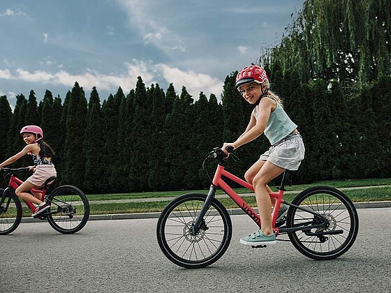 2 Mädchen auf woom Rädern am asphaltierten Radweg