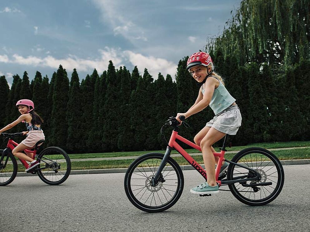 2 Mädchen auf woom Rädern am asphaltierten Radweg