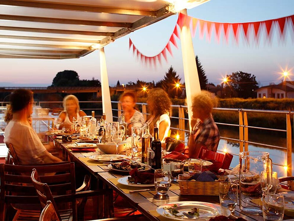Personen am Oberdeck am gedeckten Tisch in der Abenddämmerung
