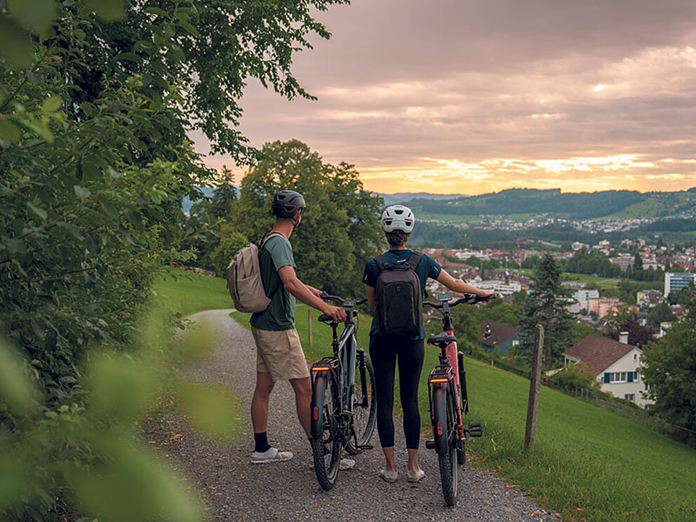2 Radfahrer auf einer Anhöhe. Sie blicken auf den Ort und halten ihre Räder fest.