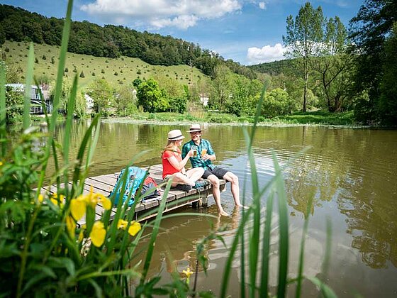 2 Radfahrer sitzen auf einem Steg und lassen die Beine in den Fluss hängen