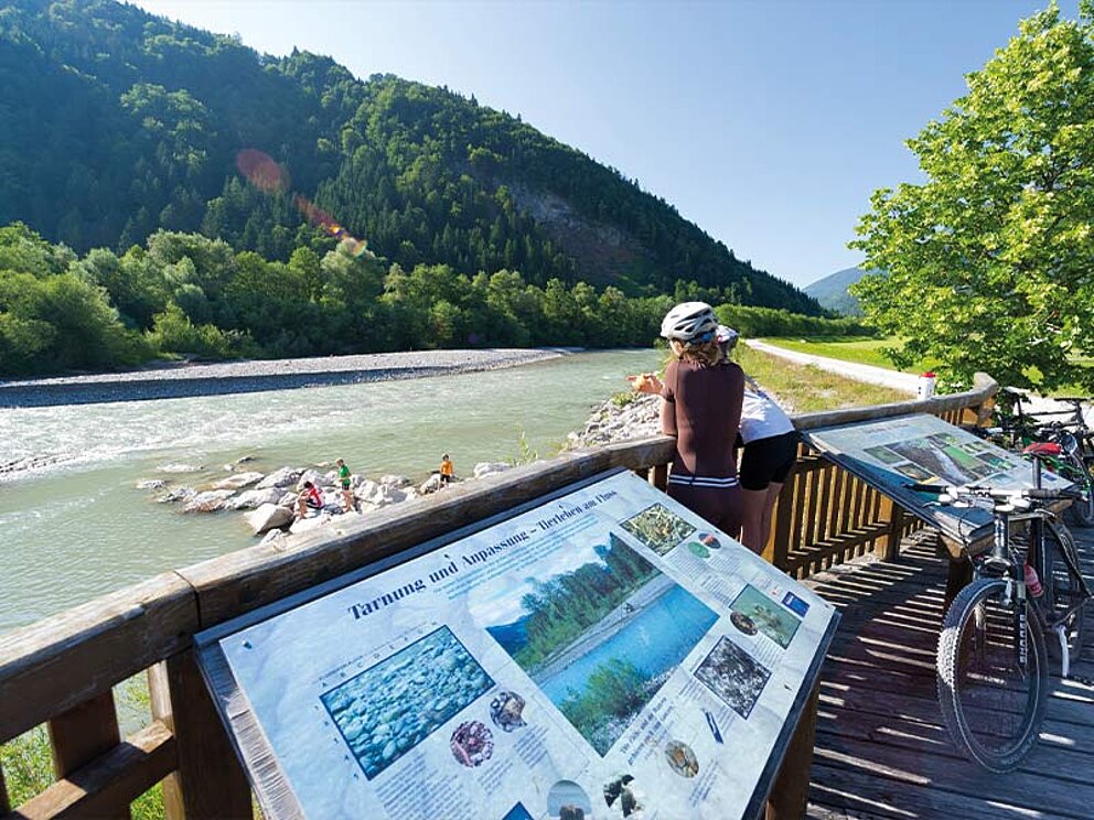 2 Personen in Radkleidung blicken auf den Inn von einer Aussichtsplattform aus.