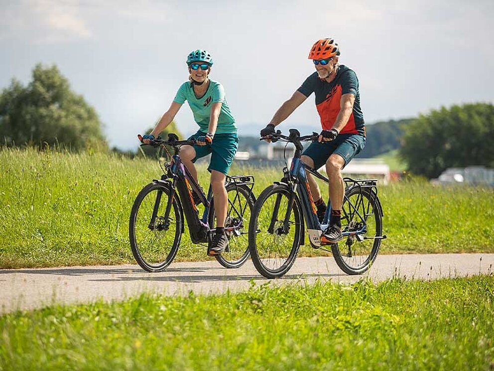 2 Radfahrer auf E-Bikes am asphaltierten Radweg