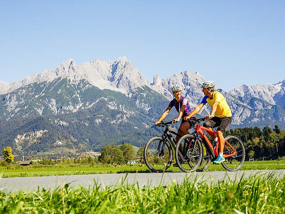 2 cyclists on ther way. Alpine range in the back, meadows in the front