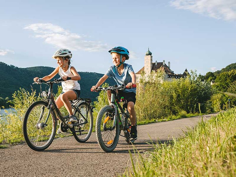 Bub und Mädel radeln am Radweg vor Schloss Schönbühel