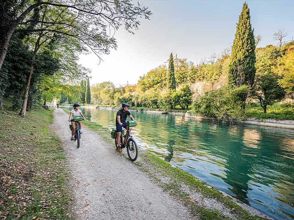 2 Radfahrer am Schotterweg am Ufer eines Flusses