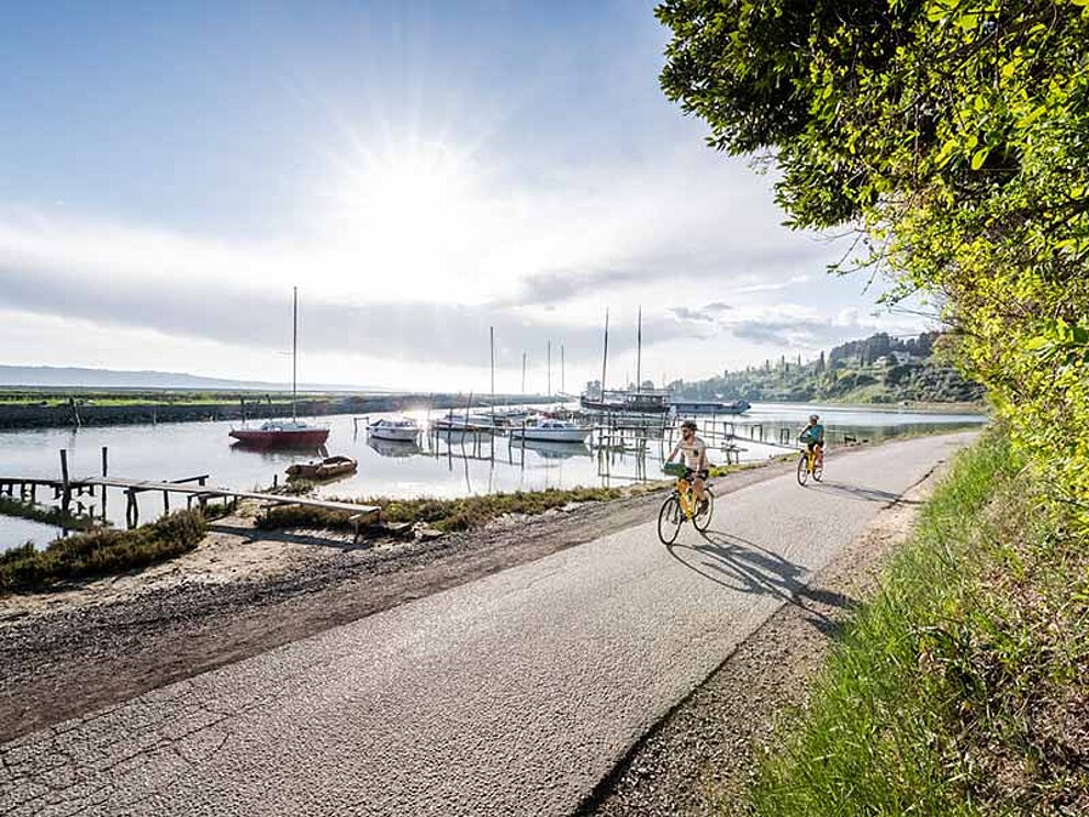 2 Radfahrer an der Küste, im Hintergrund Boote