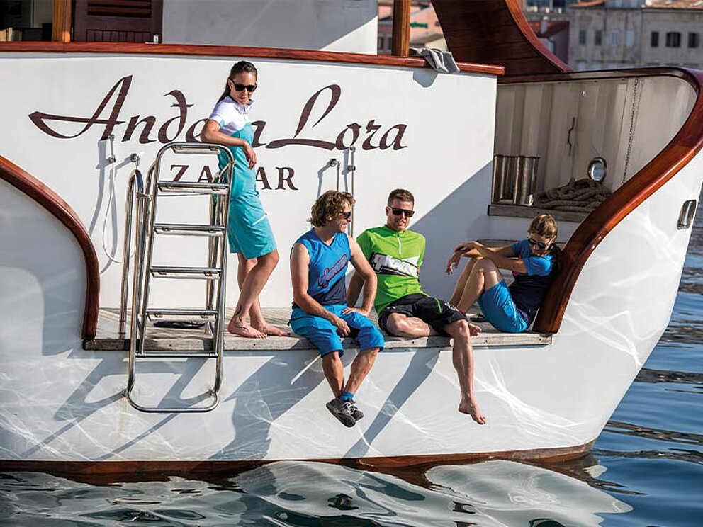 4 Personen sitzen auf der Badeplattform am Heck der Andela Lora und unterhalten sich.