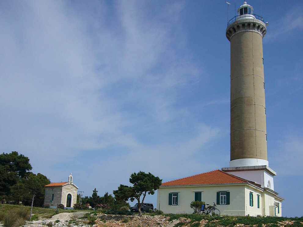 Ein Leuchtturm, davor ein kleines Häuschen und ein Fahrrad
