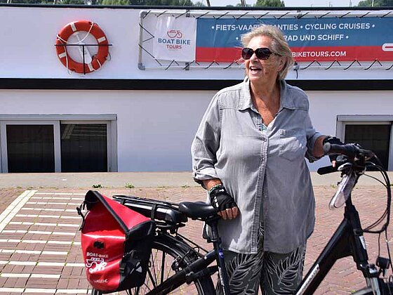 Eine ältere Frau mit Fahrrad steht am Pier, direkt vor dem Schiff