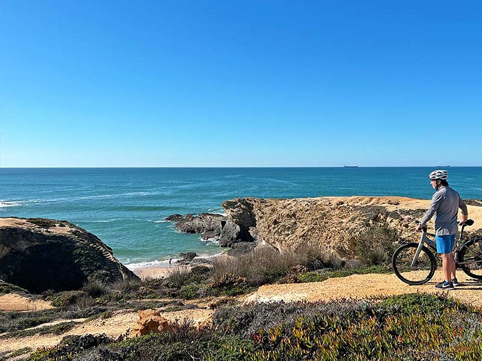 Ein Radfahrer schaut über die Klippen der portugiesischen Küste an der Algarve
