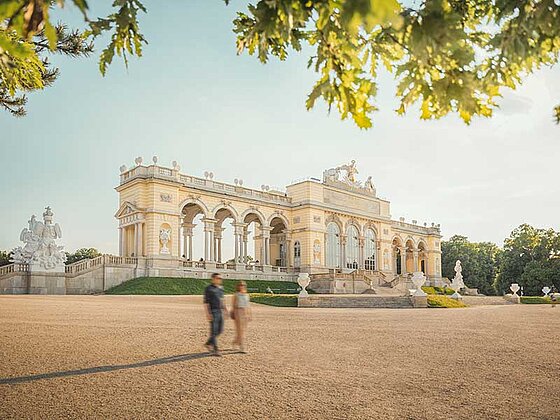 Die Gloriette im Schlosspark von Schönbrunn mit einem jungen Paar davor.