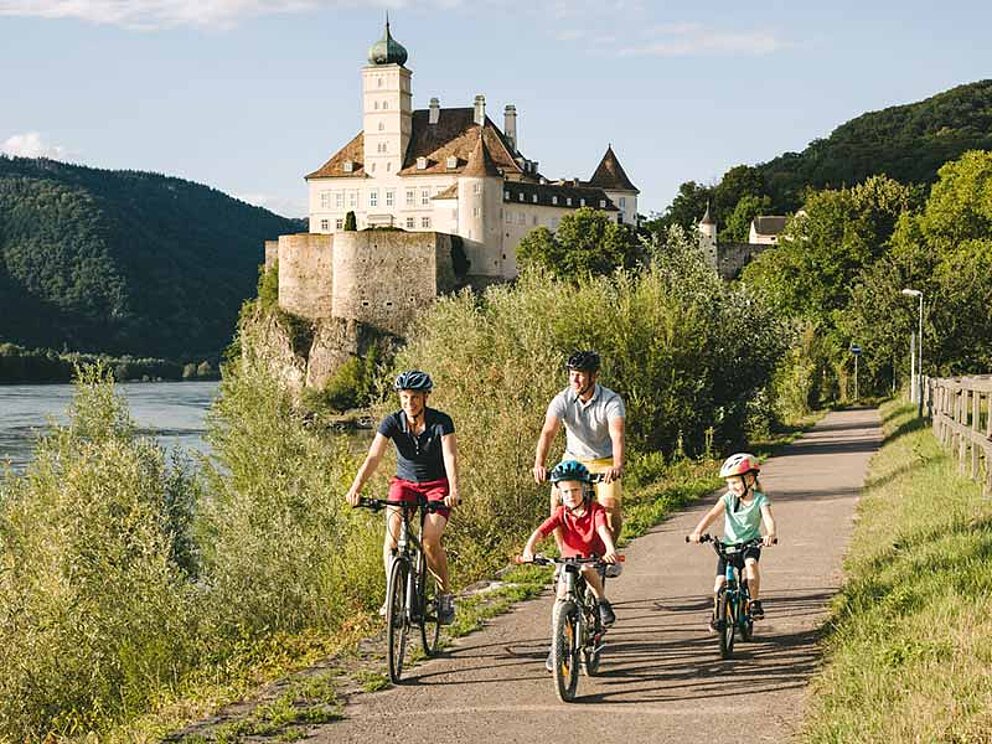 Eltern und Kinder radeln am Radweg vor Schloss Schönbühel