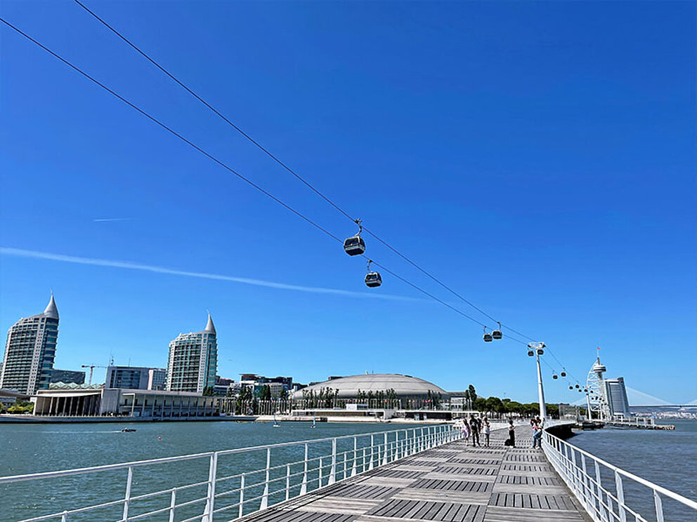 ein Steg, darüber eine Seilbahn, im Hintergrund die Skyline von Lissabon mit dem Expo-Gebäude