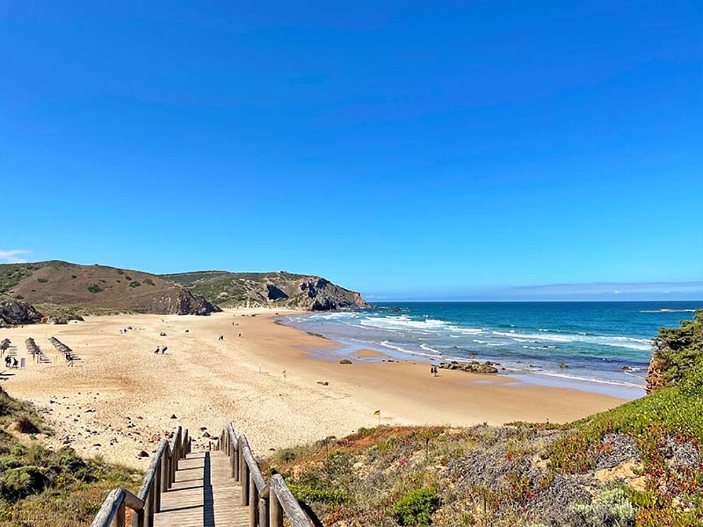 ein Steg führt in die Bucht mit Sandstrand