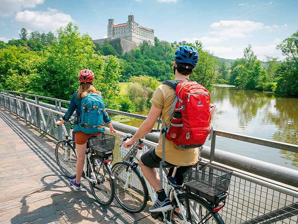 2 Radfahrer von hinten, an ein Brückengeländer gelehnt. Im Hintergrund die Willibaldburg.
