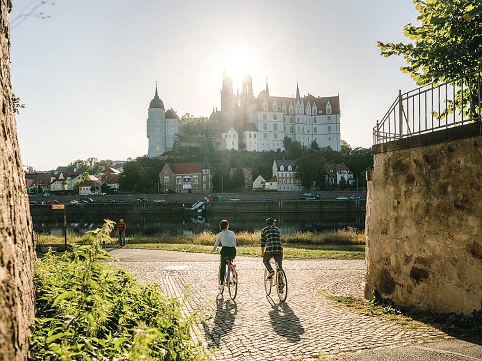 2 Radfahrer am Elbe-Ufer, im Hintergrund die STadt Meissen