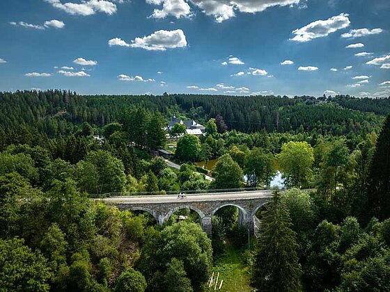 Ein ehemaliges Eisenbahn Viadukt, auf dem Radfahrer radeln. Wiesen und Wälder sowie ein Fluss sind zu sehen.