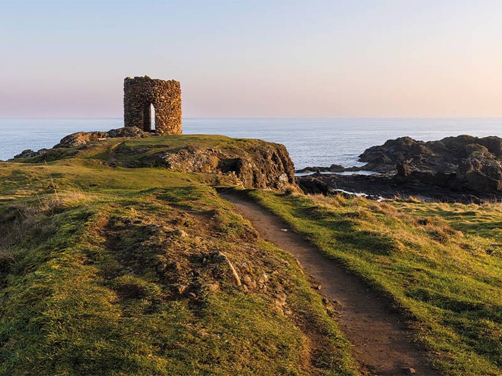 Ein Turm an der Küste, im Hintergrund Meer in der Abenddämmerung.