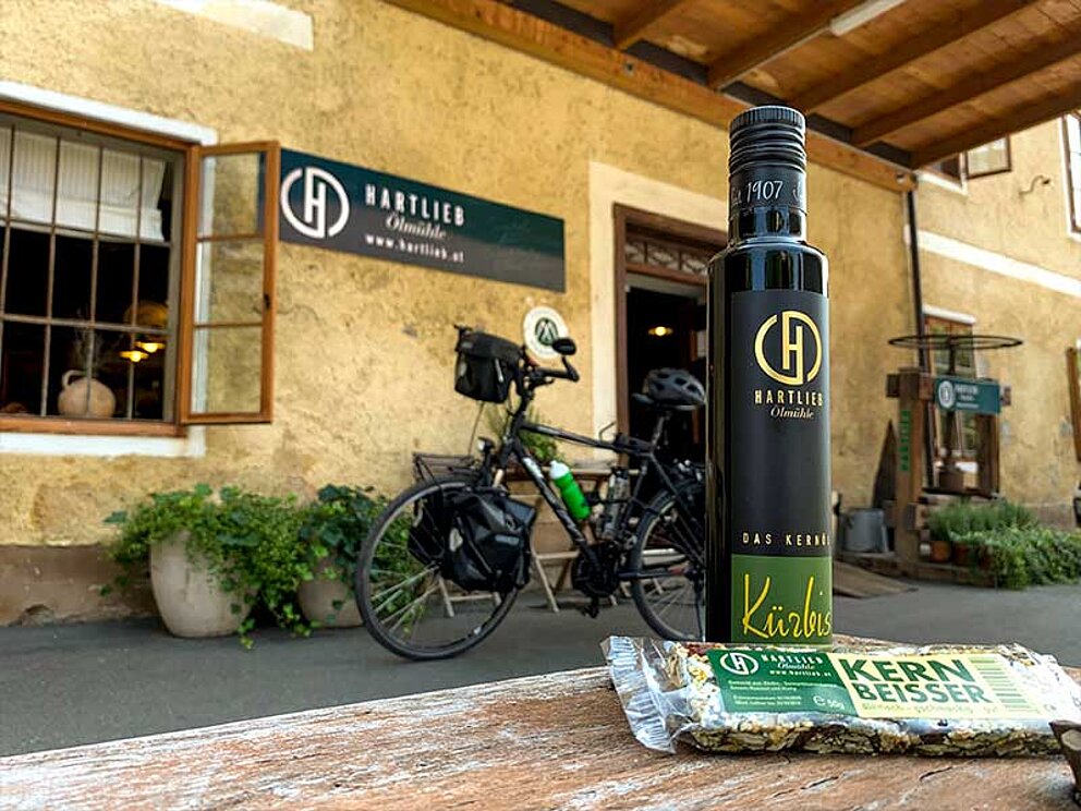  1 Flasche Kürbiskernöl auf einem Holztisch vor dem Eingang zur Ölmühle Hartlieb.