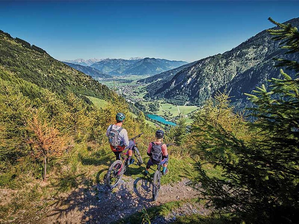 2 Biker auf einer Plattform mit Blick auf den Zeller See und die umliegende Bergwelt