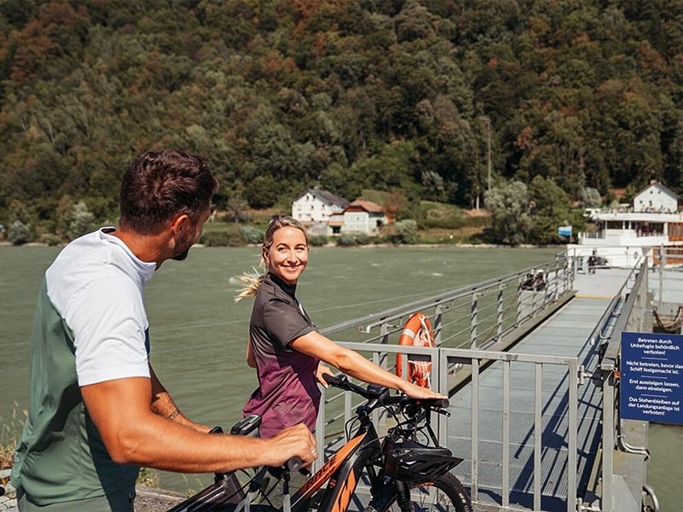 Ein Paar schiebt ihr Fahrrad in Richtung Schiffsanlegestelle in Engelhartszell