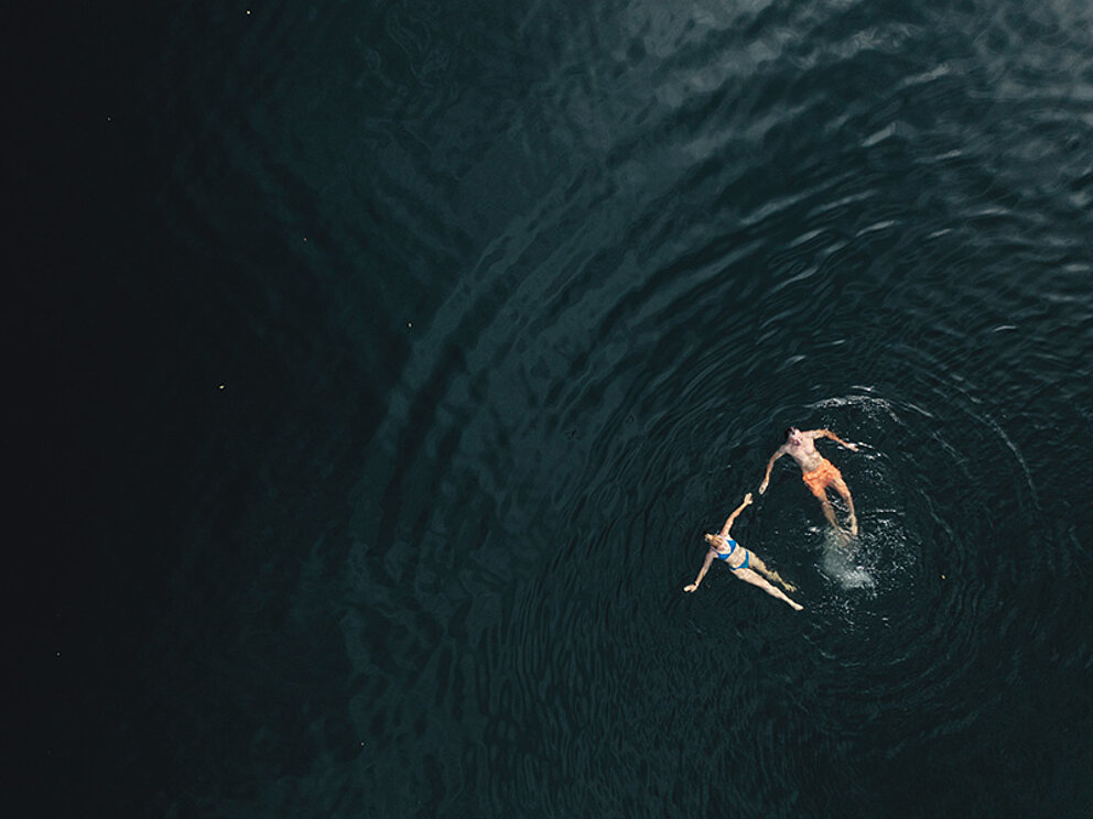 2 Personen schwimmen im See.