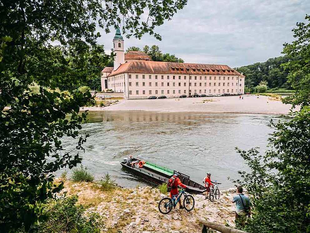 2 Radfahrer schieben ihr Rad zur Zille, im Hintergrund das Kloster Weltenburg.