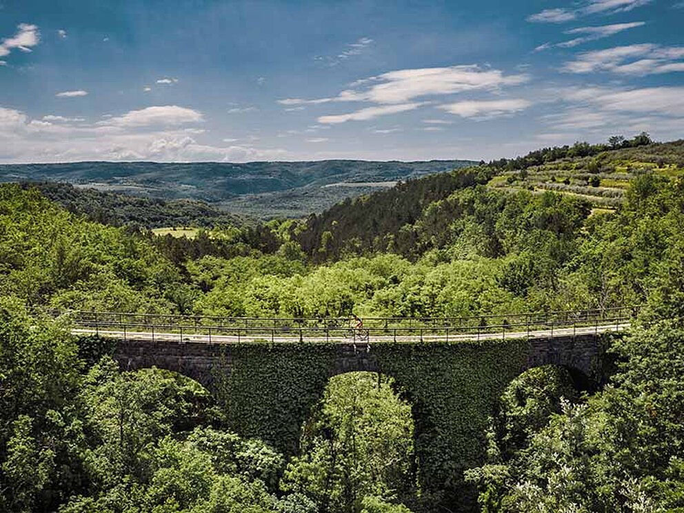 Luftaufnahme einer alten Eisenbahnbrücke, darauf sind Biker