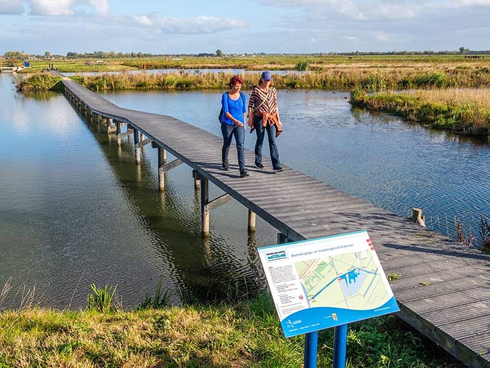 2 Damen spazieren am Steg über dem Wasserspeicher und Uberschwemmungsgebiet