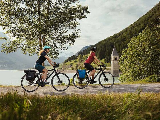 2 Radfahrer mit Satteltaschen am Rad fahren am asphaltierten Radweg vorbei am Reschensee