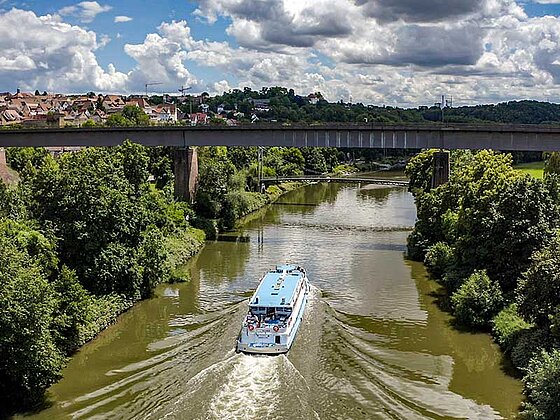 Ein Schiff fährt gemächlich am Neckar. Beide Ufer sind dicht bewaldet