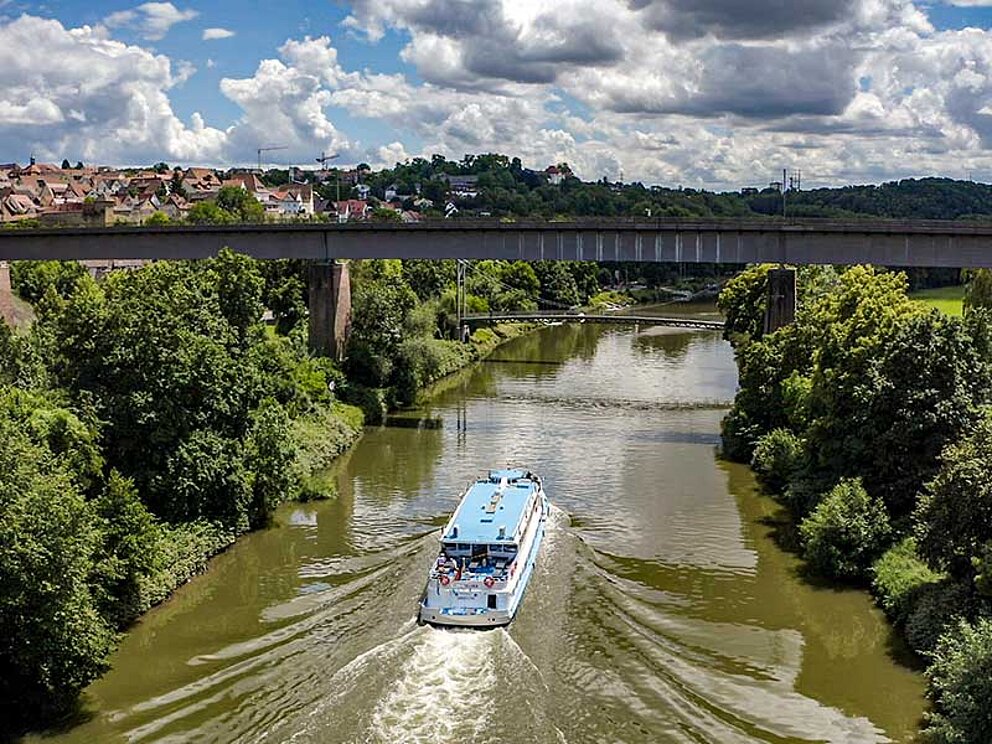 Ein Schiff fährt gemächlich am Neckar. Beide Ufer sind dicht bewaldet