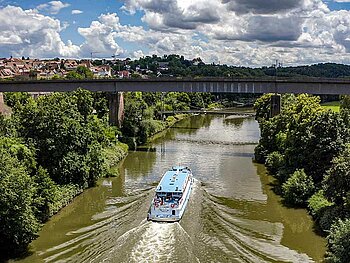 Ein Schiff fährt gemächlich am Neckar. Beide Ufer sind dicht bewaldet