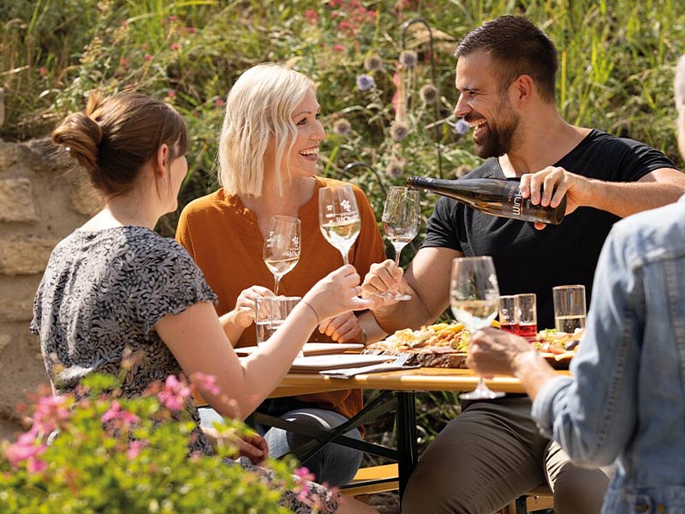 4 Personen am gedeckten Tisch mit Heurigen-Jause und Wein