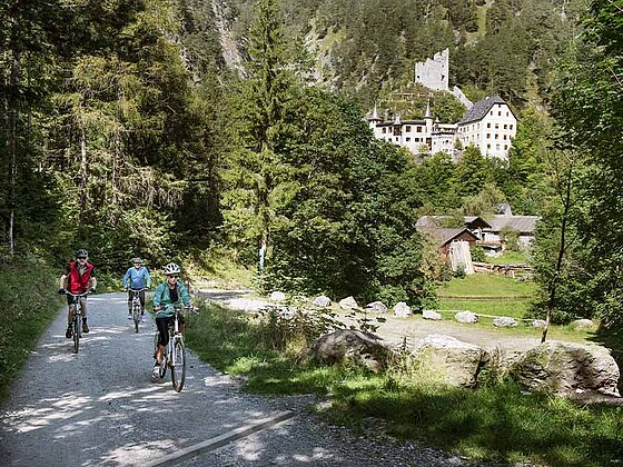 3 Radfahrer am Schotterweg, im Hintergrund ein Schloss
