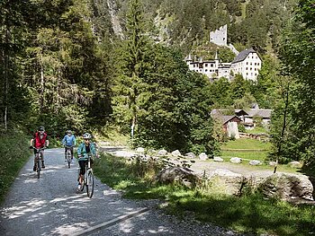 3 Radfahrer am Schotterweg, im Hintergrund ein Schloss