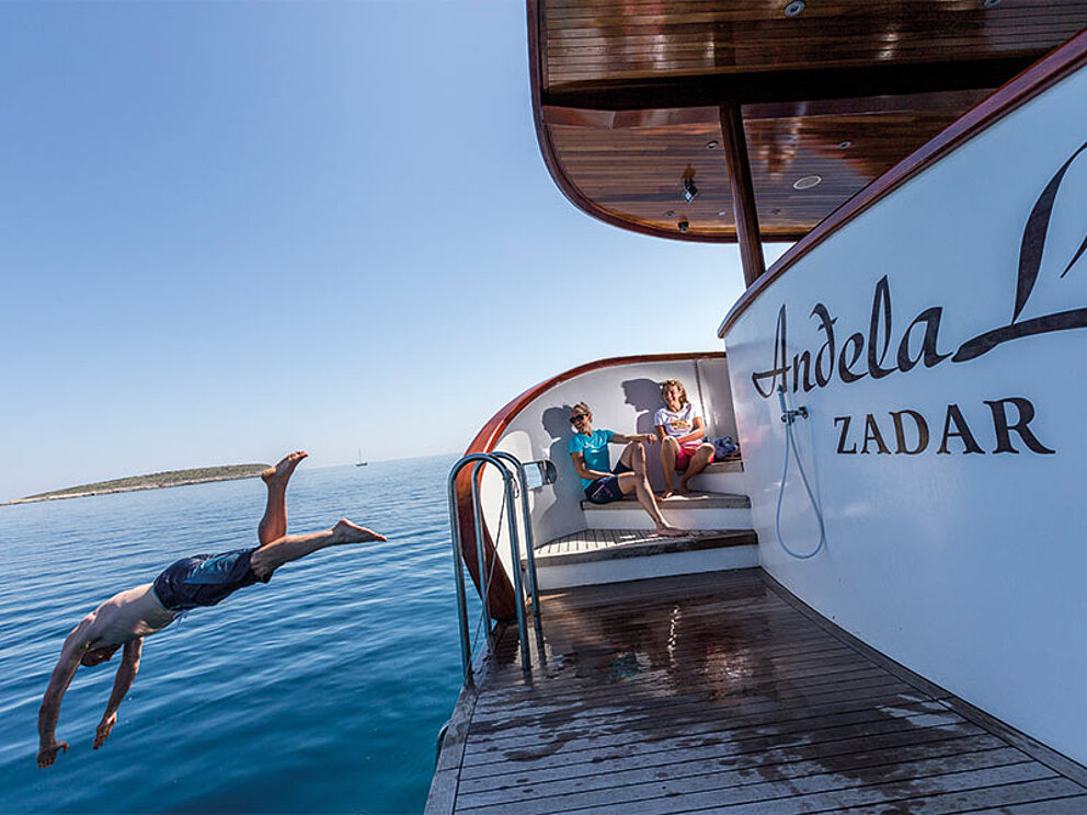 Ein Mann springt ins Meer von der Badeplattform am Heck der Andela Lora