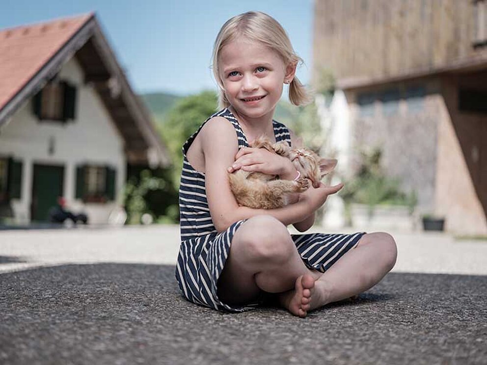 kleines Mädchen sitzt mit Katze am Boden 