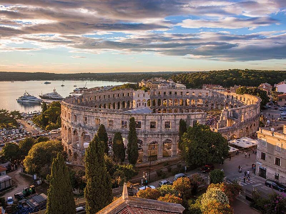 Luftaufnahme der Arena von Pula in der Abenddämmerung, im Hintergrund das Meer