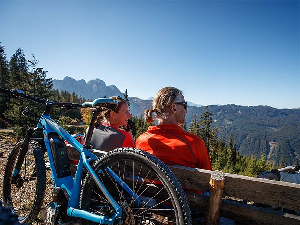 Mountainbiker rasten auf einer Holzbank und genießen den Blick in die Ferne.