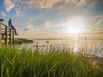 Frau genießt vom Steg aus Sonnenaufgang auf der Insel Amrum am Strand
